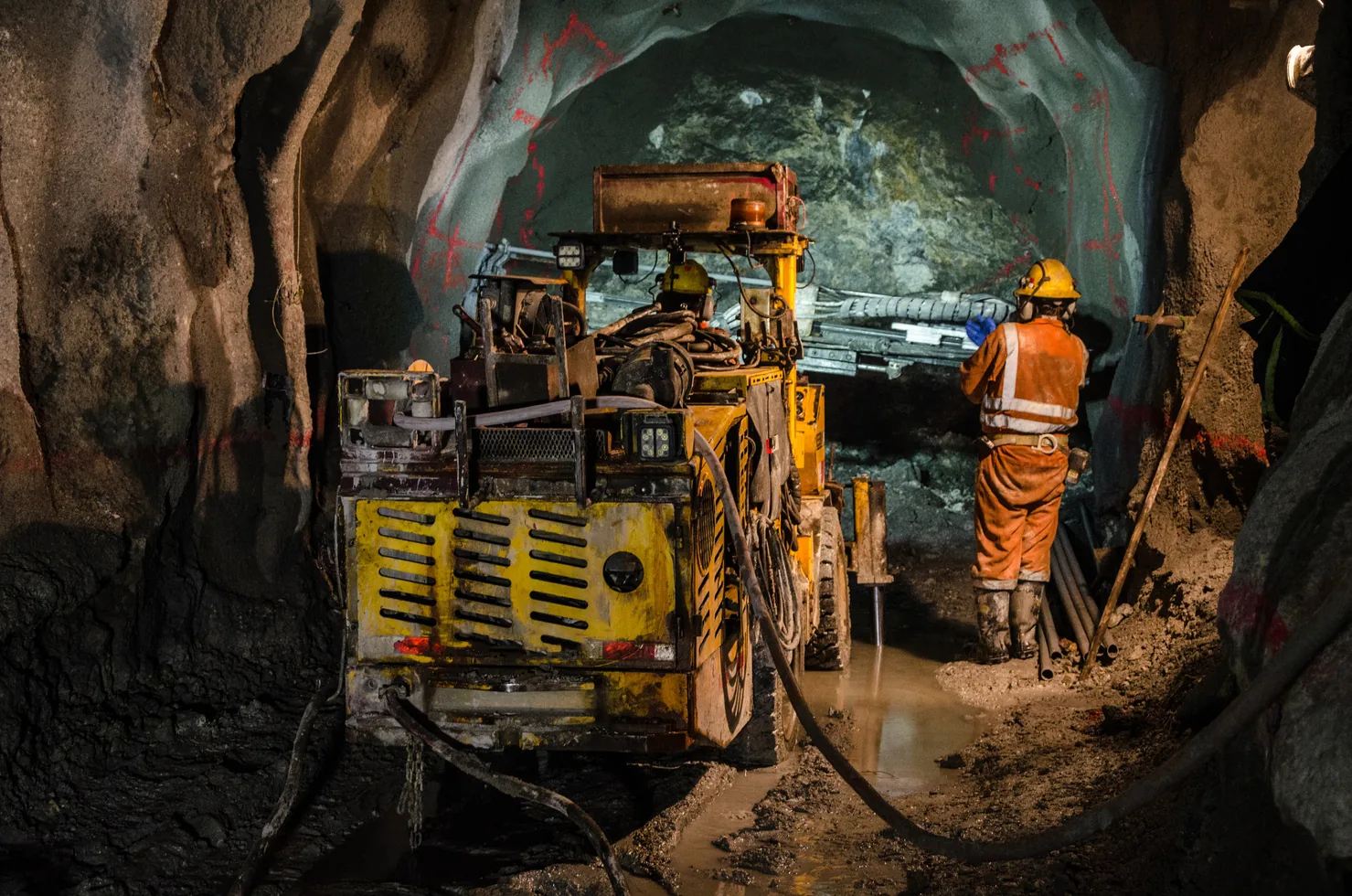 A drill rig and an operator in high-visibility clothing working in an underground mine tunnel