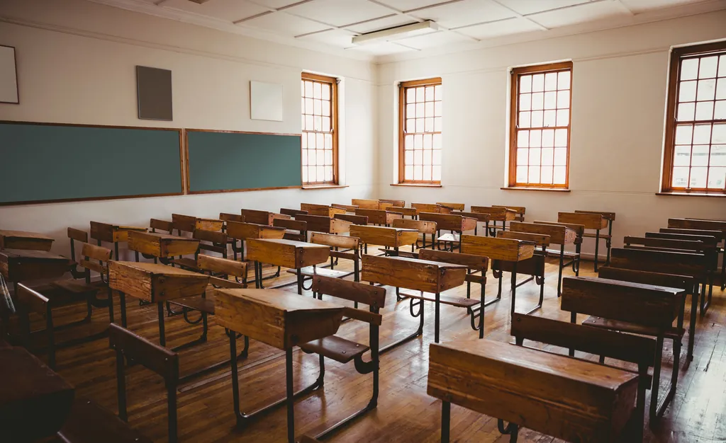 An empty classroom with rows of wooden desks facing a chalkboard
