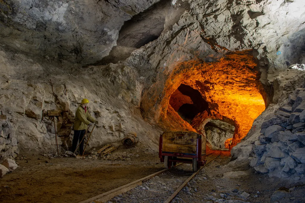 An underground mine tunnel lit orange, with a miner beside an ore cart on rails